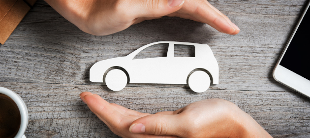 Deux mains protègent une voiture de papier déposée sur une table en bois.