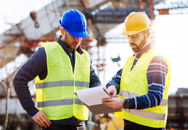 Deux entrepreneurs regardent une planchette à pince sur un chantier de construction.