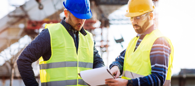 Deux entrepreneurs regardent une planchette à pince sur un chantier de construction.