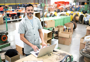 Un homme regarde l’écran d’un ordinateur portable dans un entrepôt avec des produits en arrière-plan.