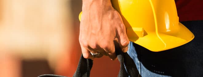 Un travailleur de la construction tenant une boîte à outils et un casque.