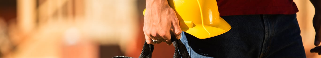 Un travailleur de la construction tenant une boîte à outils et un casque.