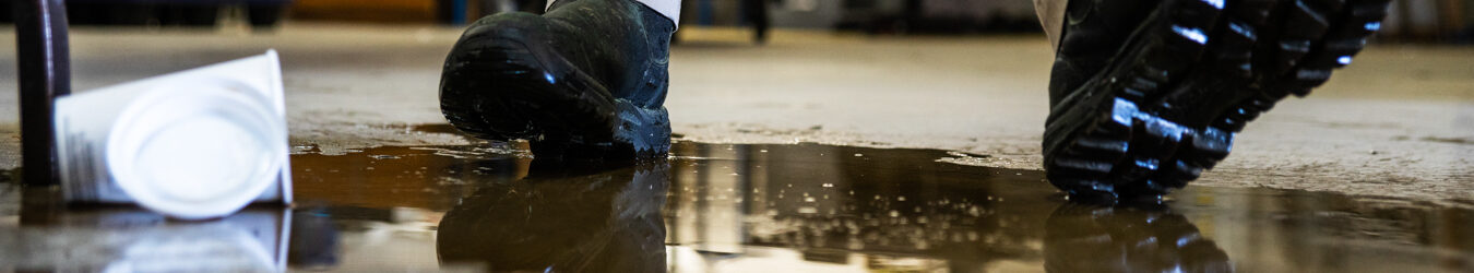 Un travailleur dans un entrepôt marchant dans un liquide renversé.