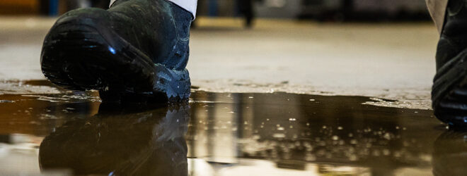 Un travailleur dans un entrepôt marchant dans un liquide renversé.